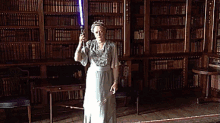 a woman in a white dress is holding a blue light saber in a library