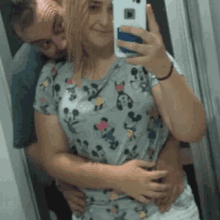 a man is hugging a woman while she takes a selfie in the mirror .
