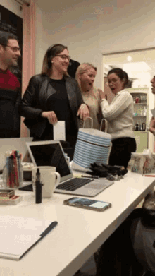 a group of people standing around a table with a laptop and a cell phone