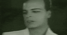 a close up of a man 's face in a black and white photo . he is wearing a white shirt and tie .
