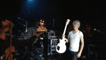 a man holding a guitar stands next to a man holding a cake