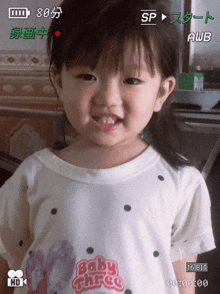 a little girl wearing a white shirt that says baby three on it