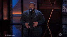 a man singing into a microphone with nbc written on the bottom