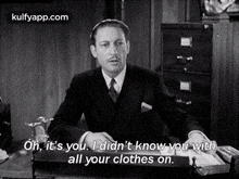 a man in a suit and tie is sitting at a desk and talking to another man .