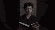 a young man is reading a book in front of a brick wall