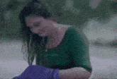 a woman in a green shirt and purple gloves is sitting at a table with her hair wet .