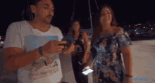 a man and two women are standing next to each other at night . the man is holding a cell phone .