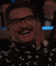 a man with glasses and a beard is wearing a shirt with letters on it