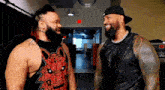 two wrestlers are standing next to each other in a hallway and smiling at each other .
