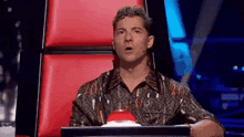 a man sitting in a chair with his mouth open and a red button in front of him