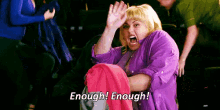 a woman in a purple shirt is screaming and holding a pink shirt in her hands .