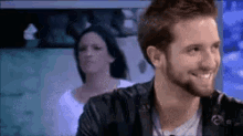 a man with a beard is smiling with a woman behind him .
