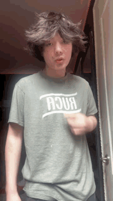 a young man wearing a green aqua t-shirt stands in front of a door