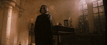 a man in a black cape stands in a dark room with candles