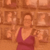a woman in a purple dress and glasses is standing in front of a wall of pictures of women .