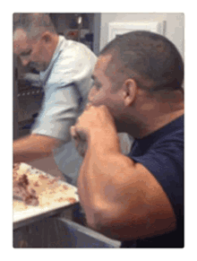 two men are cooking in a kitchen and one is eating food