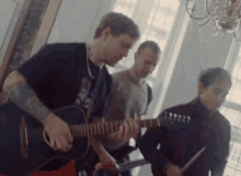 a man is playing a guitar while two other men play drums
