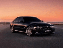 a black bmw is parked on the side of a road at sunset