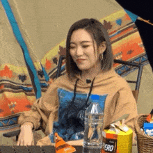 a woman is sitting in a chair in front of a tent with a bottle of water and a bag of chips .
