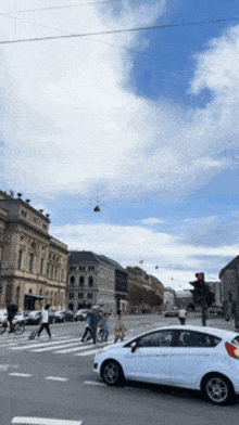 a white car is driving down a street with people crossing