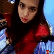 a girl in a red shirt is sitting on a bed with a gif me logo in the corner