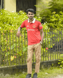 a man wearing a red teamviewer shirt stands next to a fence