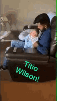a man is sitting in a chair holding a baby in his lap .