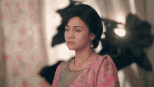 a woman wearing a pink top and a necklace looks sad