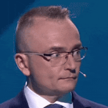 a man in a suit and tie with glasses and a microphone in his ear .