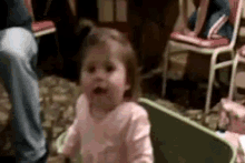 a baby girl in a pink shirt is standing next to a green table .