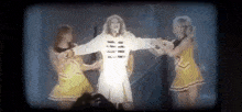 a woman is singing into a microphone while two cheerleaders are standing behind her .