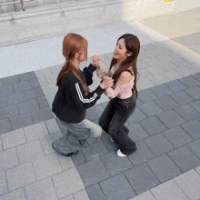 two girls are dancing on a sidewalk and one is wearing a black sweatshirt