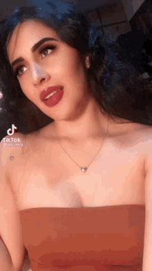 a woman wearing a necklace and a strapless top has a tiktok icon on her shoulder