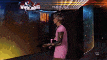 a man in a pink shirt is holding a gun in front of a wrestlemania sign
