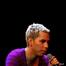 a man in a purple shirt is singing into a microphone with the words rbd.gif below him