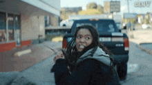 a woman with dreadlocks is standing in front of a truck with the word genv on the bottom