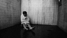 a black and white photo of a man in a straight jacket sitting on the floor .