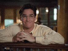 a man wearing glasses and a yellow shirt is leaning on a railing and smiling
