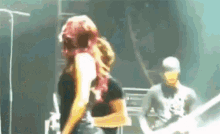 a woman with red hair is standing on a stage with a man playing a guitar