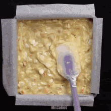 a purple spatula is being used to spread a batter in a pan that says mr.cakes on the bottom