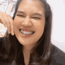 a woman with braces is smiling with her eyes closed and her hand on her face .