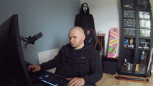 a man sits in front of a computer in a room with a scream mask in the background