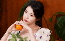 a woman making a heart shape with her hands holding an orange