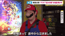 a man in a mario costume stands in front of a welcome to the super mario bros movie poster