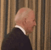 a man in a suit and white shirt is standing in front of a curtain .