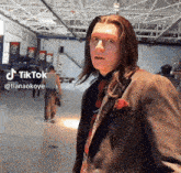 a man with long hair is wearing a suit and tie and has a tiktok icon above his head