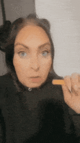 a woman in a black hoodie is holding a small piece of food in her hand .