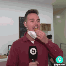 a man wearing a face mask holds a microphone with the letter a on it in front of a sign that says croquetes