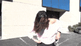 a woman wearing a pink off the shoulder top is standing in a parking lot