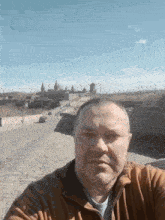 a man in a brown jacket is taking a selfie with a city in the background